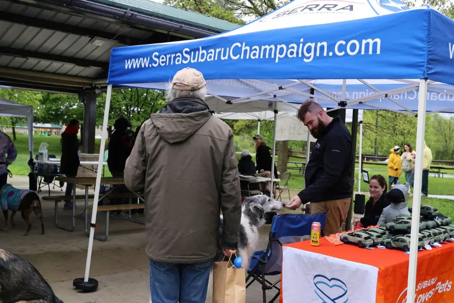 An event guest and his borzoi dog meet a Subaru employee under the SerraSubaruChampaign.com Tent at Mutt Strut 2025